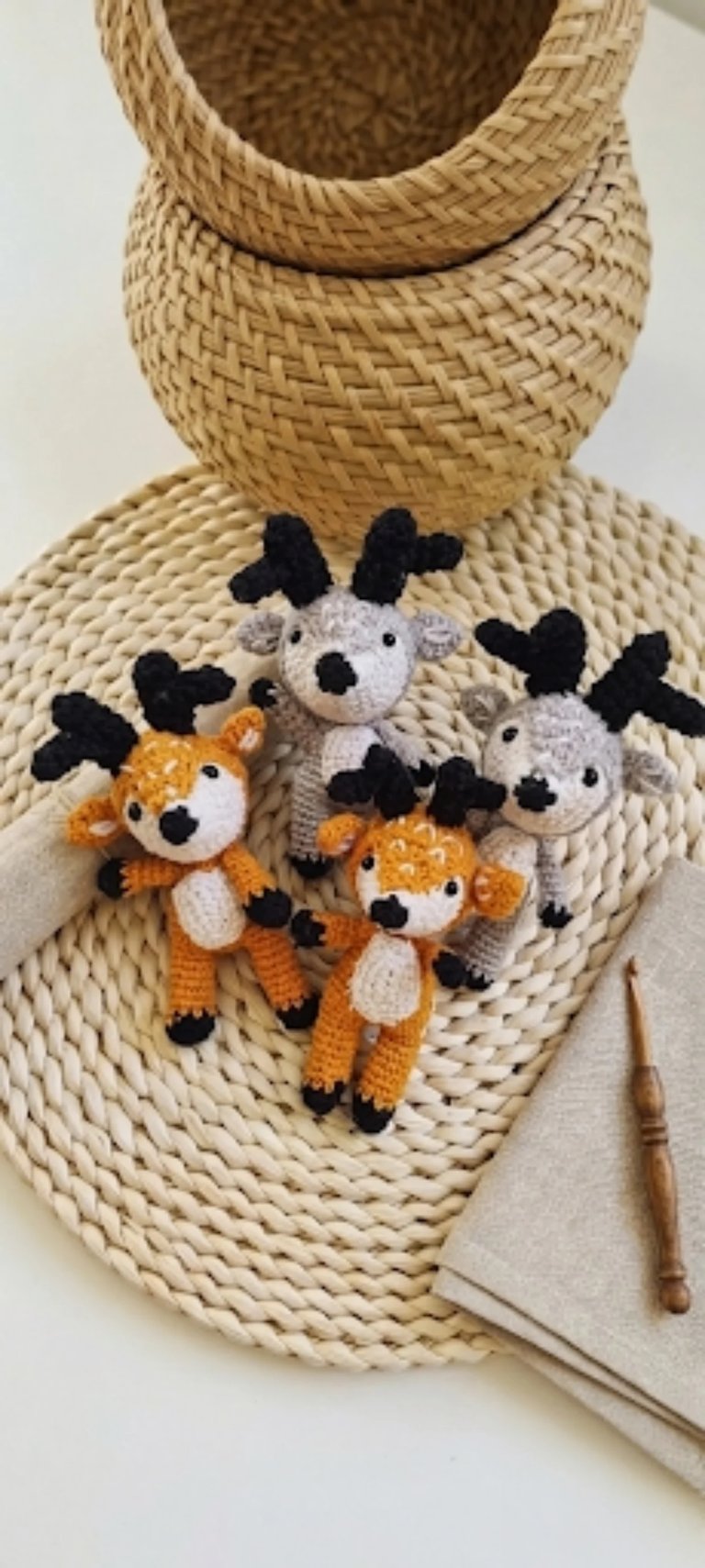Four crocheted animal toys with black and white or orange features displayed on a beige woven basket, alongside knitting needles and yarn