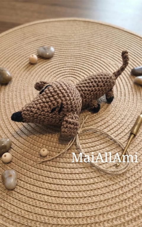 Crocheted tan dinosaur amigurumi toy on a circular woven placemat with decorative beads and a tail