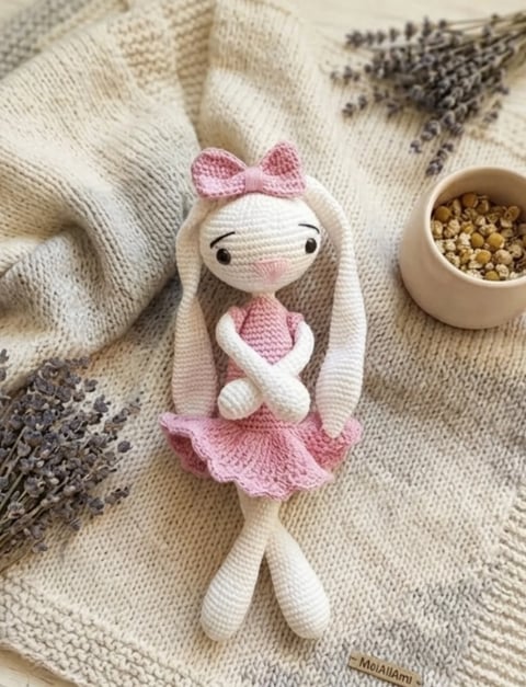 Crocheted bunny doll with pink bow and skirt on cream knit fabric, surrounded by dried lavender and decorative items