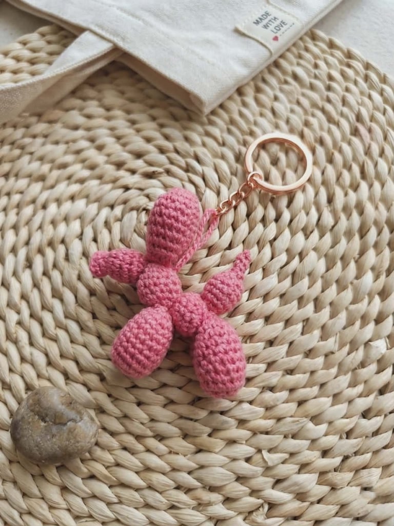 Pink crocheted cactus keychain on a woven natural straw placemat with folded white fabric nearby