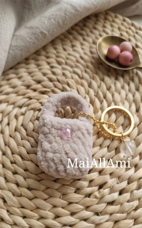 Handmade pink crocheted pouch with charm on woven placemat, next to ceramic bowl with decorative beads