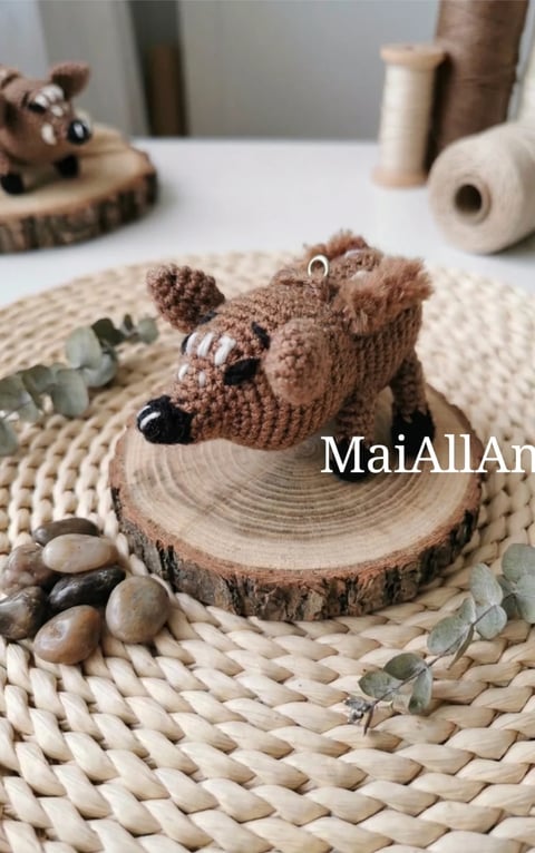 Handmade brown crocheted raccoon figurine sitting on a wood slice, surrounded by decorative stones and dried eucalyptus