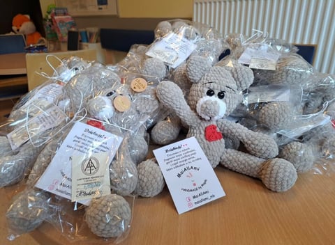 Homemade crocheted stuffed animals wrapped in plastic on a wooden table with handmade tags attached
