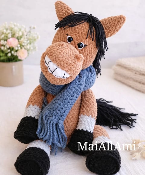 Crocheted amigurumi horse toy with brown body, black mane, white markings, blue scarf, and embroidered smile