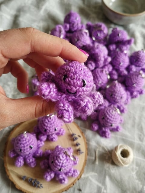 Hand holding a small purple crocheted octopus amigurumi with several others displayed on a wooden dish below