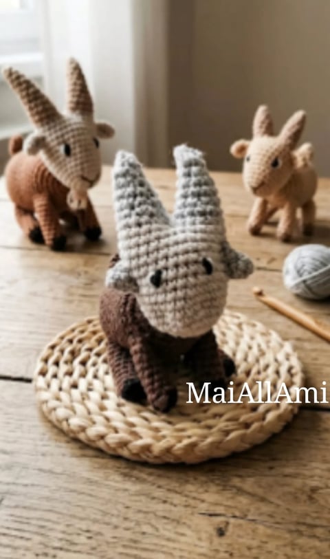 Three crocheted amigurumi goats on a wooden surface with a woven placemat and yarn ball