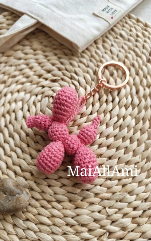 Pink crocheted cactus keychain on woven placemat with folded white cloth nearby