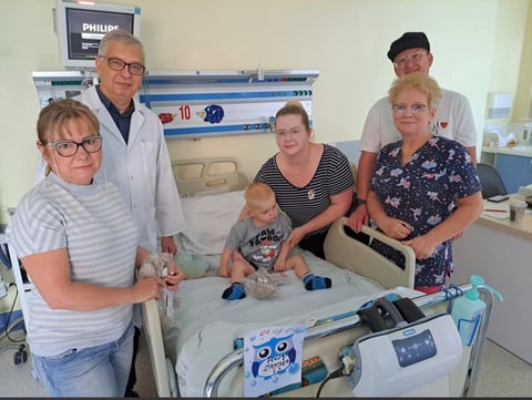 Five people gathered around a medical incubator in a hospital room, examining a newborn baby