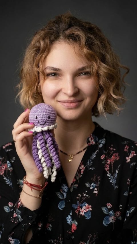 Young woman with curly brown hair smiling while holding a small crocheted purple octopus toy