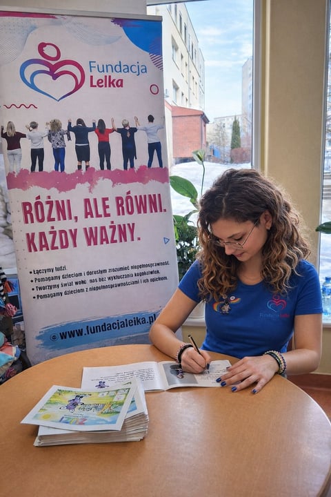Woman signing documents at a table in front of a Fundacja Lelka charitable organization banner