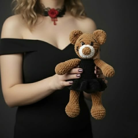 Woman in black off-shoulder dress holding a brown teddy bear with white snout, wearing red rose choker necklace against dark background