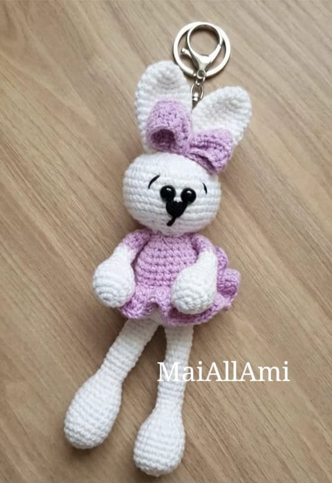 Crocheted amigurumi rabbit keychain with white body, lavender bow and dress, featuring a heart nose and long dangling legs